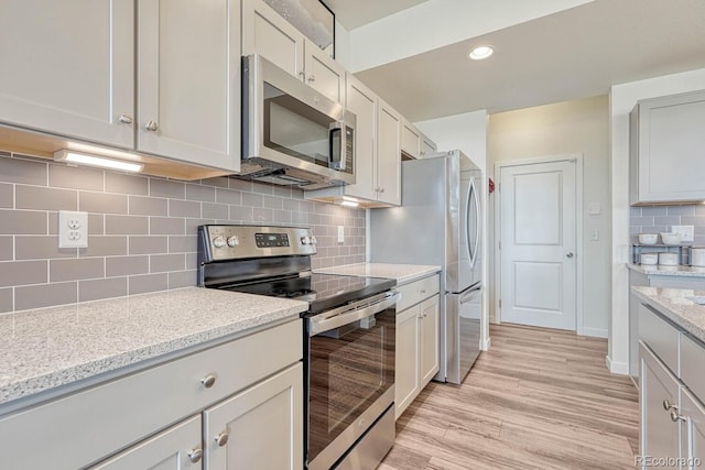 kitchen featuring light stone counters, white cabinets, appliances with stainless steel finishes, light wood-type flooring, and tasteful backsplash