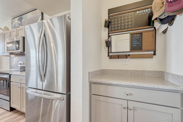 kitchen with light wood-type flooring, appliances with stainless steel finishes, decorative backsplash, and light stone counters