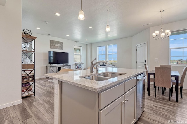 kitchen featuring dishwasher, hanging light fixtures, a sink, and a center island with sink