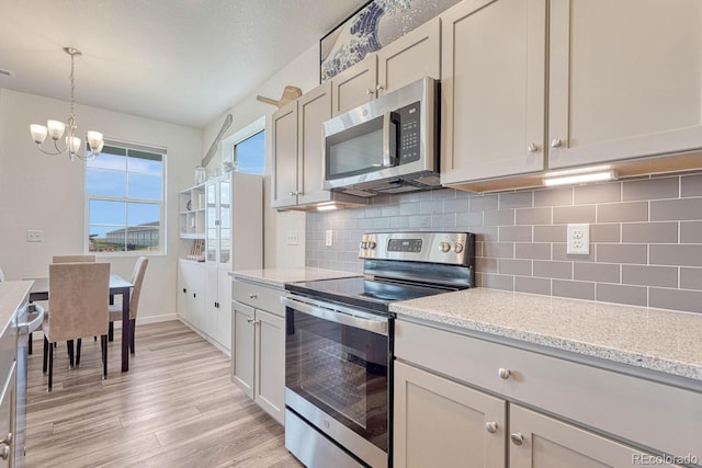 kitchen with decorative light fixtures, tasteful backsplash, appliances with stainless steel finishes, light stone countertops, and light wood-type flooring