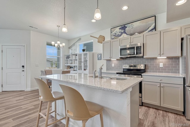 kitchen featuring pendant lighting, appliances with stainless steel finishes, a kitchen island with sink, and light stone countertops