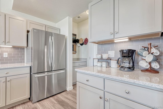 kitchen with visible vents, freestanding refrigerator, light stone countertops, light wood-type flooring, and backsplash