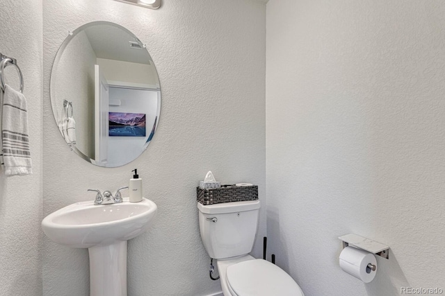 half bath with toilet, a sink, and a textured wall