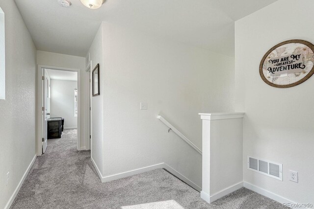 hall with baseboards, visible vents, light carpet, and an upstairs landing