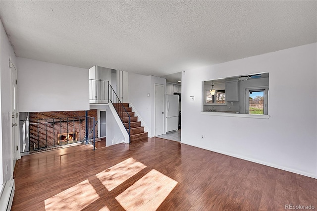 1796 S Yampa Way, Aurora, CO 80017 - unfurnished living room with stairs, wood finished floors, a textured ceiling, a fireplace, and baseboard heating