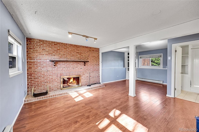 1796 S Yampa Way, Aurora, CO 80017 - unfurnished living room with baseboard heating, a textured ceiling, a brick fireplace, wood finished floors, and baseboards