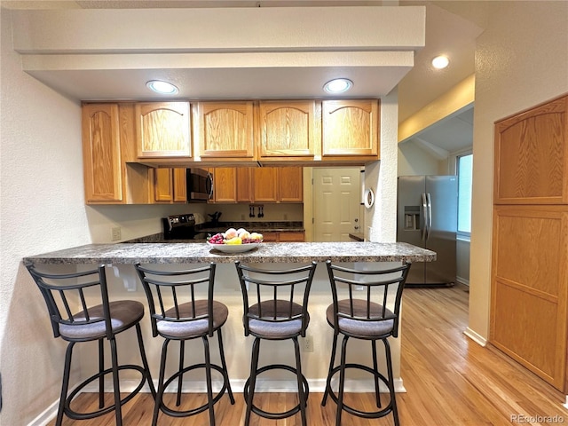 4493 Dunkirk Way, Denver, CO 80249 - kitchen featuring appliances with stainless steel finishes, a peninsula, light wood-style floors, a breakfast bar area, and a textured wall
