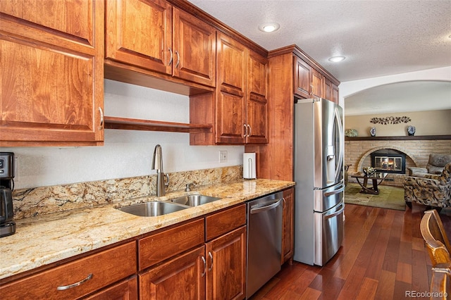 kitchen with sink, appliances with stainless steel finishes, dark hardwood / wood-style floors, a fireplace, and light stone countertops