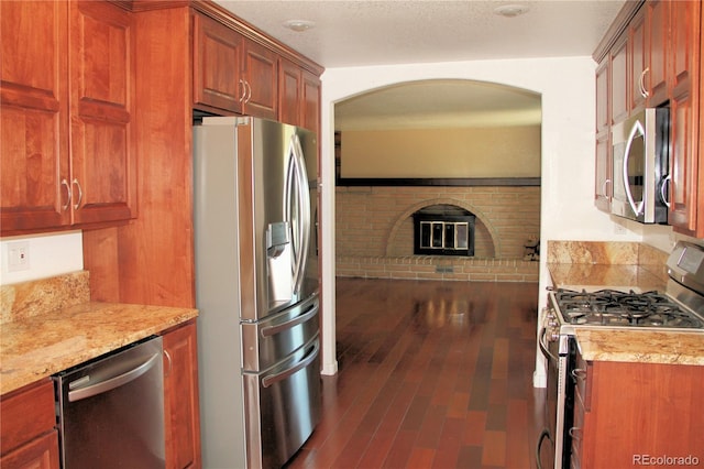 7891 Poplar St, Commerce City, CO 80022 - kitchen featuring stainless steel appliances, arched walkways, dark wood finished floors, a brick fireplace, and brown cabinets