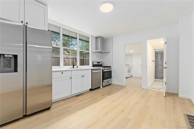 kitchen featuring wall chimney exhaust hood, white cabinets, light hardwood / wood-style flooring, and stainless steel appliances