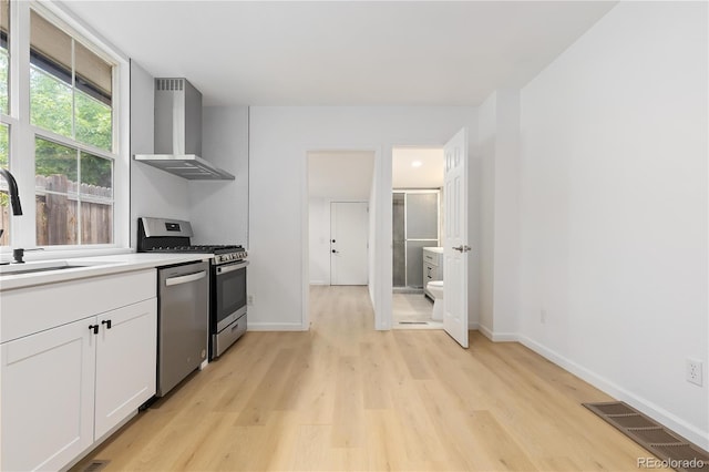 kitchen featuring light hardwood / wood-style floors, wall chimney range hood, stainless steel dishwasher, and range