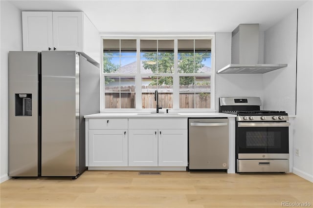 kitchen with sink, light hardwood / wood-style flooring, white cabinetry, stainless steel appliances, and wall chimney range hood