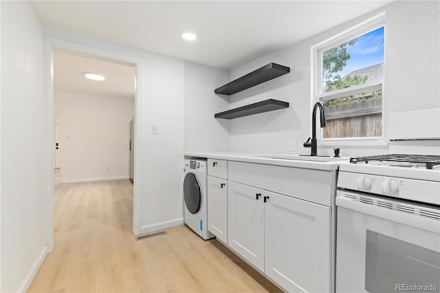 kitchen featuring light wood-type flooring, gas range gas stove, washer / dryer, white cabinets, and sink