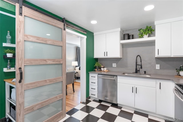 kitchen with light floors, open shelves, a barn door, appliances with stainless steel finishes, and a sink