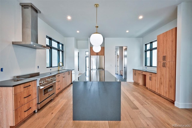 kitchen featuring sink, pendant lighting, stainless steel appliances, light hardwood / wood-style floors, and wall chimney range hood