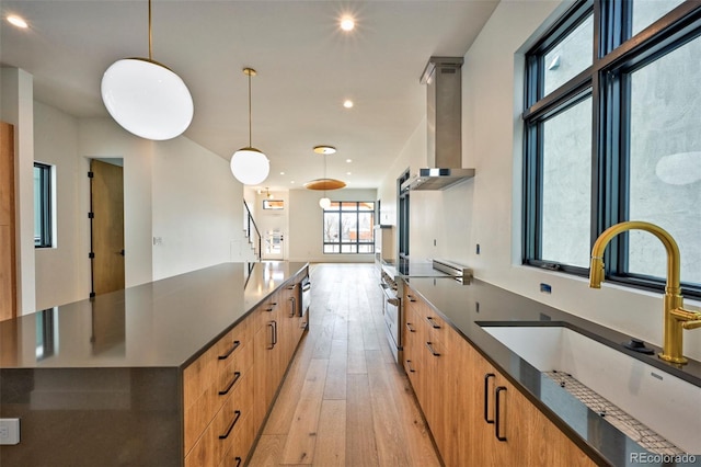 kitchen featuring wall chimney exhaust hood, sink, decorative light fixtures, light wood-type flooring, and stainless steel range