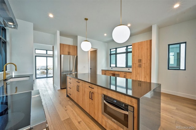 kitchen with a kitchen island, pendant lighting, sink, stainless steel appliances, and light hardwood / wood-style flooring