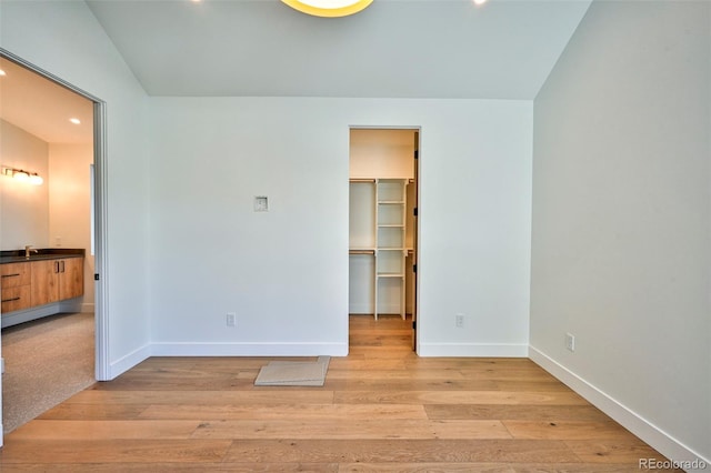 unfurnished bedroom featuring connected bathroom, sink, a spacious closet, light wood-type flooring, and a closet