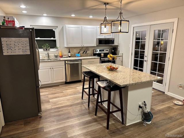 kitchen with a center island, sink, hanging light fixtures, stainless steel appliances, and white cabinets