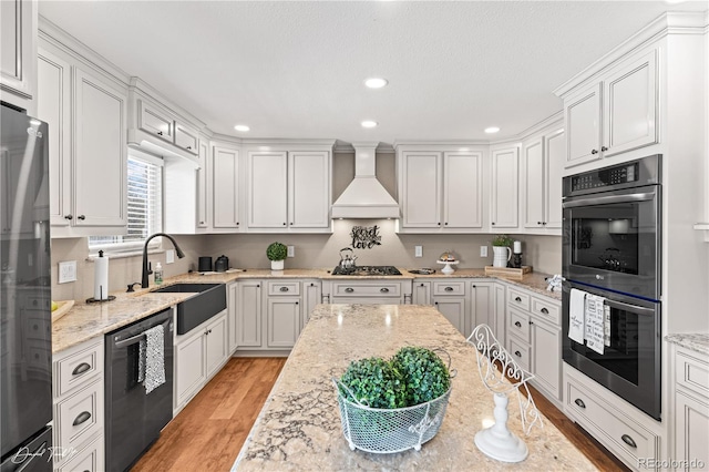 kitchen featuring premium range hood, light stone counters, stainless steel appliances, sink, and white cabinetry