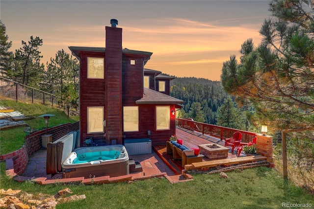 back house at dusk featuring a hot tub, an outdoor fire pit, and a wooden deck