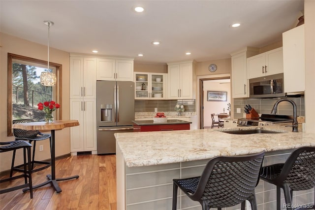 kitchen featuring kitchen peninsula, appliances with stainless steel finishes, light wood-type flooring, pendant lighting, and white cabinets