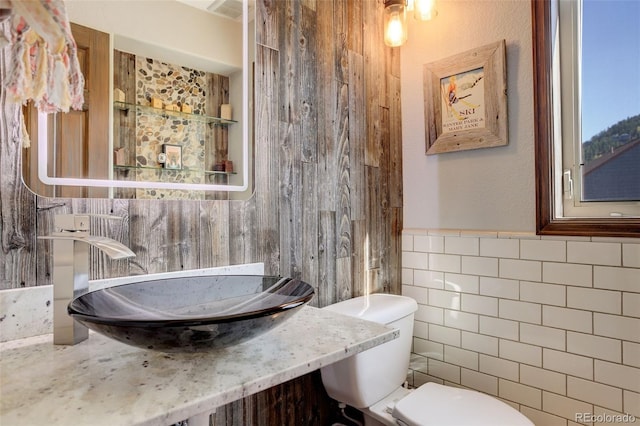 bathroom with toilet, tile walls, and sink