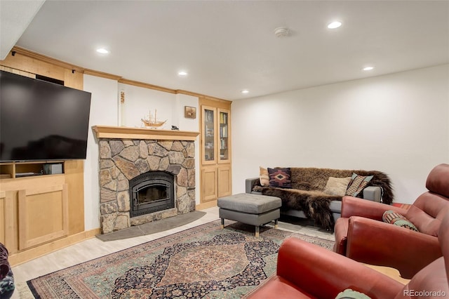 living room with a stone fireplace, ornamental molding, and light wood-type flooring