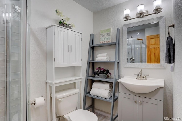 bathroom featuring vanity, wood-type flooring, toilet, a textured ceiling, and a shower with shower door