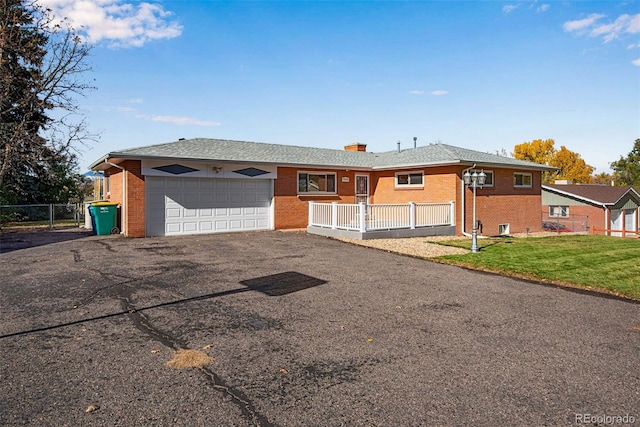 single story home featuring aphalt driveway, an attached garage, brick siding, fence, and a front yard