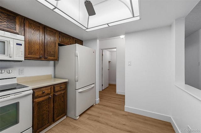 kitchen with dark brown cabinetry, white appliances, baseboards, light countertops, and light wood-style flooring
