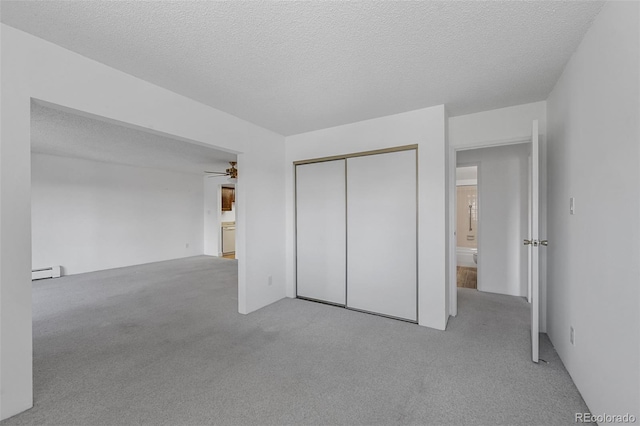 unfurnished bedroom with carpet floors, a textured ceiling, a baseboard heating unit, and a closet