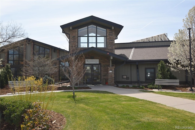 view of front of home with a front lawn, stone siding, french doors, a shingled roof, and board and batten siding