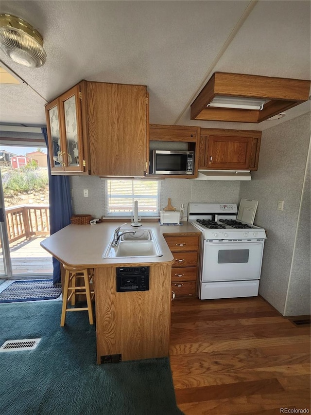 kitchen featuring a textured ceiling, dark hardwood / wood-style floors, a kitchen breakfast bar, white gas range, and sink