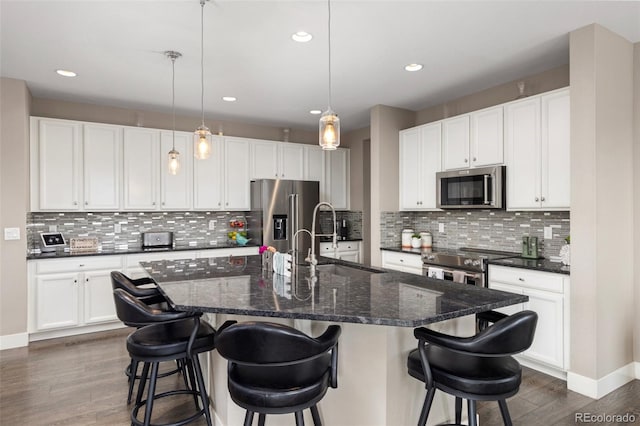 kitchen featuring pendant lighting, white cabinets, a kitchen breakfast bar, a kitchen island with sink, and stainless steel appliances