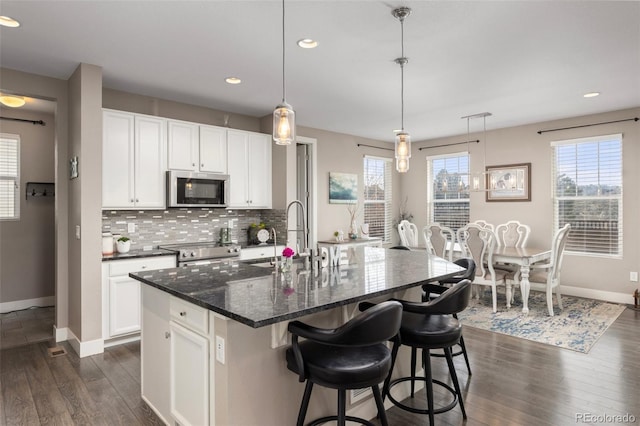 kitchen featuring sink, appliances with stainless steel finishes, white cabinetry, a center island with sink, and decorative light fixtures