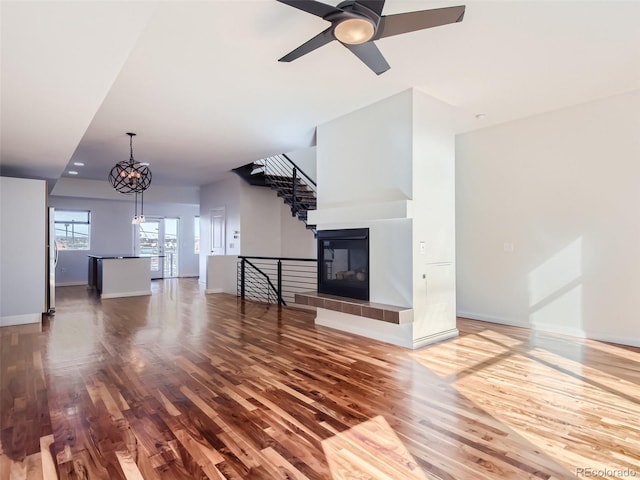 unfurnished living room featuring hardwood / wood-style flooring, a tile fireplace, and ceiling fan with notable chandelier