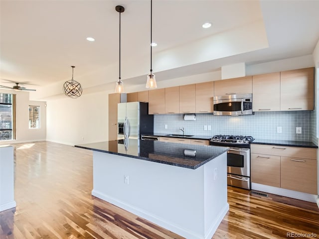 kitchen featuring a kitchen island, decorative light fixtures, stainless steel appliances, dark stone counters, and hardwood / wood-style flooring