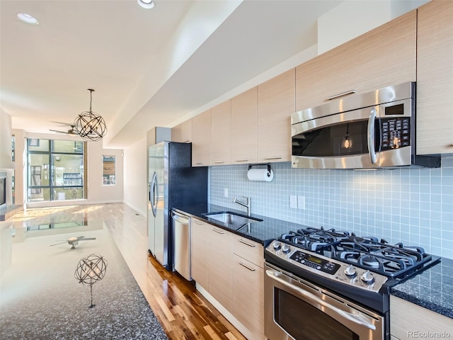 kitchen featuring appliances with stainless steel finishes, dark stone counters, sink, backsplash, and hanging light fixtures