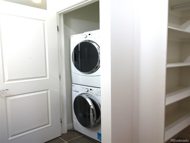 laundry area with stacked washer / dryer and dark tile patterned flooring