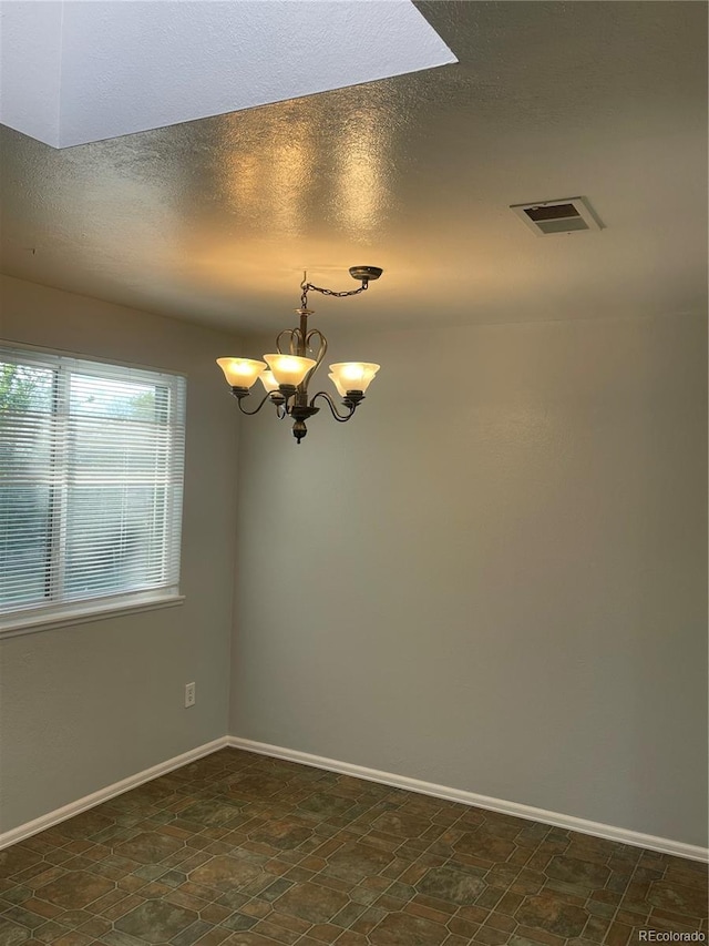 2617 S Cimarron St, Aurora, CO 80014 - spare room featuring a chandelier, baseboards, a textured ceiling, and dark stone finish flooring