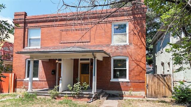 view of front facade featuring covered porch, brick siding, fence, and a gate