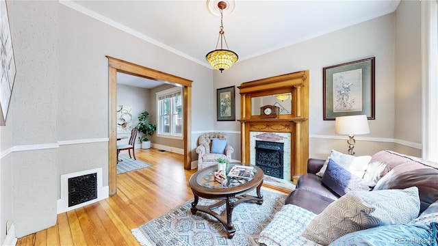 living area with crown molding, a fireplace, visible vents, wood finished floors, and baseboards