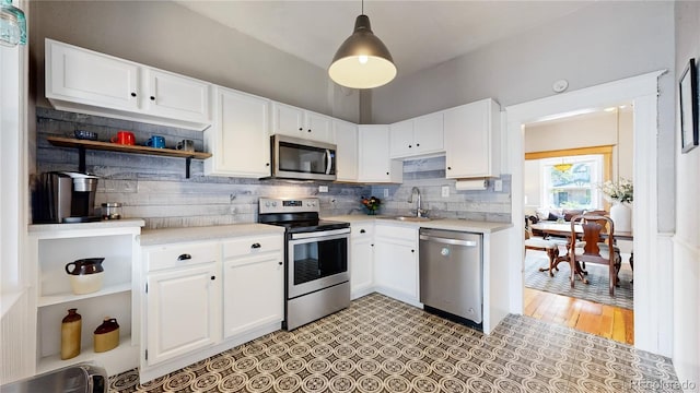 kitchen featuring appliances with stainless steel finishes, light countertops, white cabinetry, open shelves, and a sink