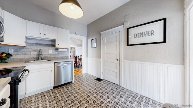 kitchen with a sink, white cabinets, stainless steel dishwasher, and wainscoting