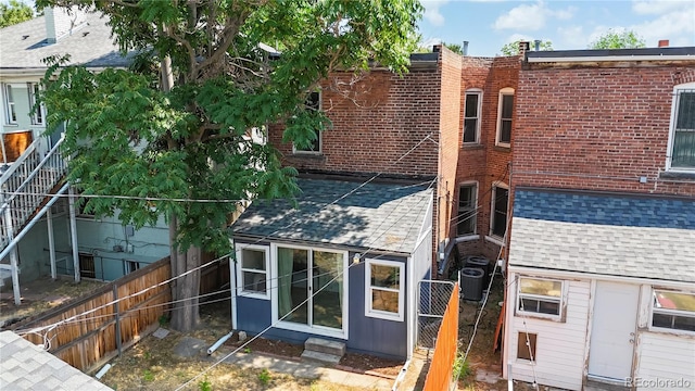 back of house with a shingled roof, brick siding, fence, and central AC unit