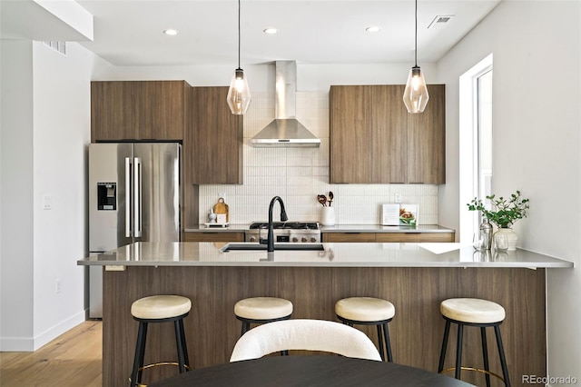 kitchen featuring wall chimney exhaust hood, light hardwood / wood-style flooring, hanging light fixtures, and a breakfast bar area