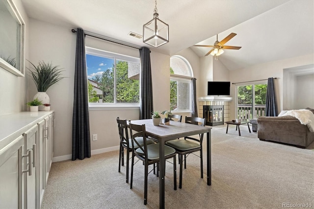 dining space with light colored carpet, ceiling fan, healthy amount of natural light, vaulted ceiling, and a fireplace