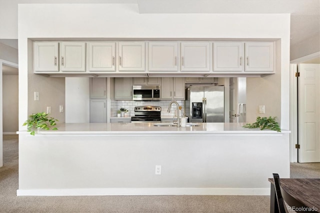 kitchen featuring stainless steel appliances, a sink, carpet, light countertops, and a peninsula