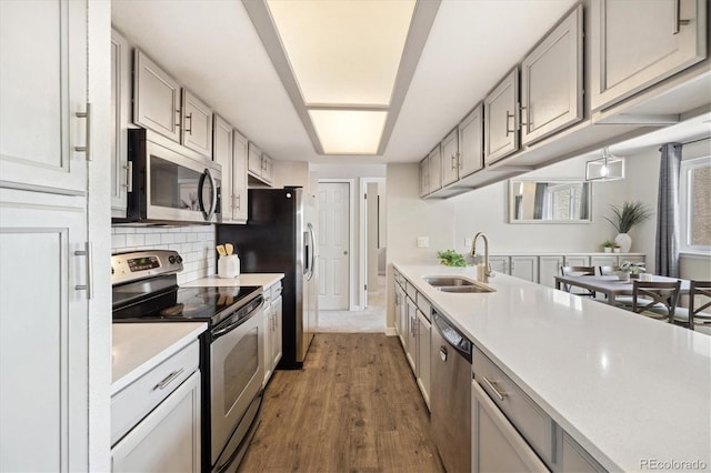 kitchen featuring a sink, stainless steel appliances, dark wood-style flooring, light countertops, and decorative backsplash